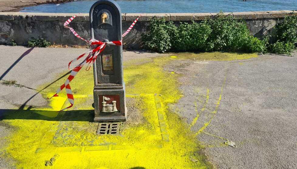Operaio lava un secchio di vernice gialla alla fontana pubblica