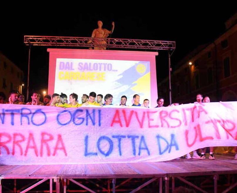 Gli azzurri di mister Alessandro Dal Canto in piazza Alberica durante la presentazione con lo striscione preparato dai tifosi della Carrarese: tifosi che ieri hanno festeggiato l’esordio vincente e storico a Cesena