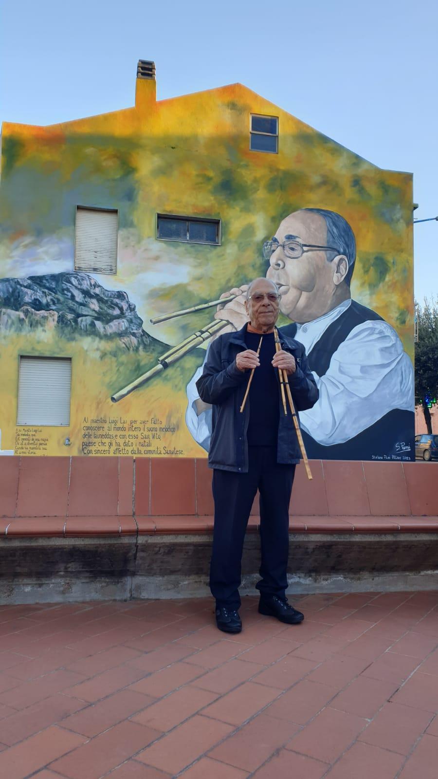 
	Il maestro Luigi Lai davanti al murale che lo ritrae

