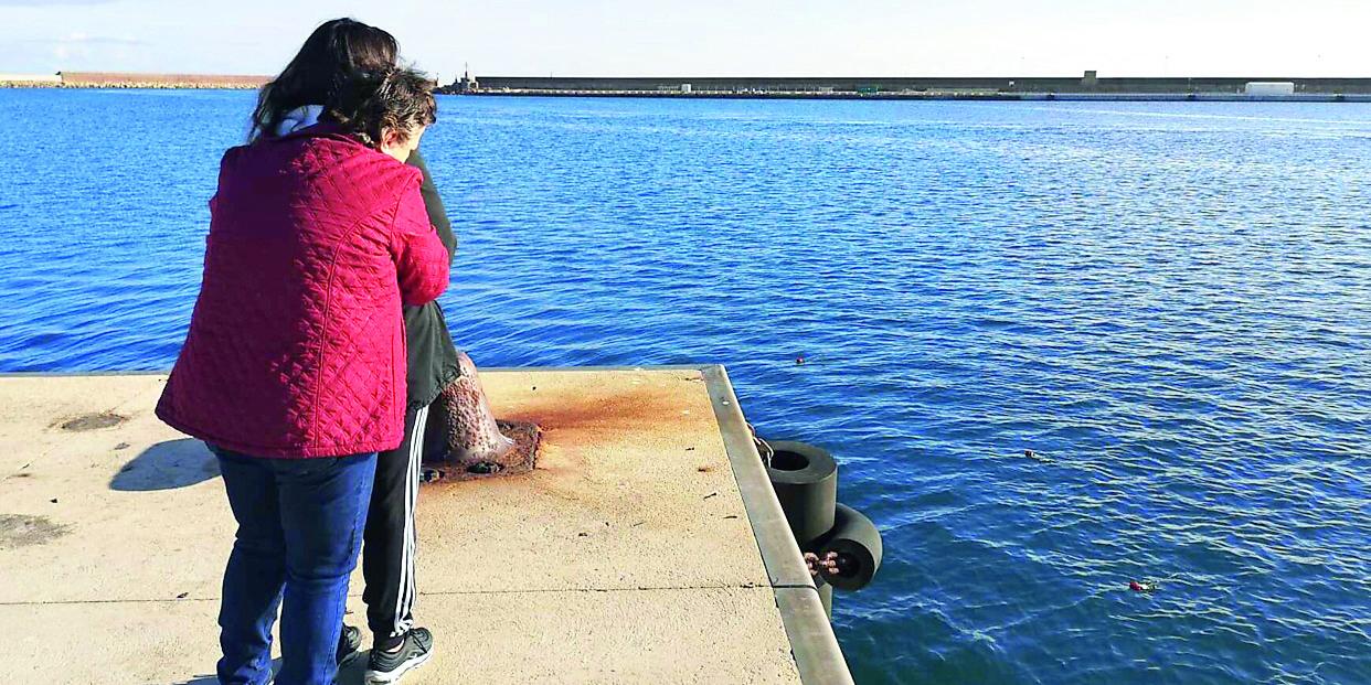 Madre e figlia abbracciate piangono commosse dopo aver lanciato in mare le rose rosse per ricordare l'amato marito e padre