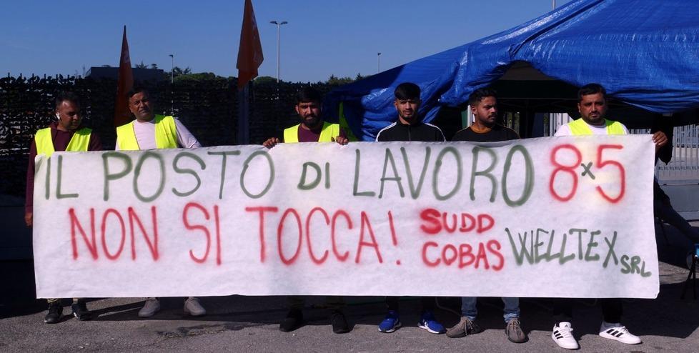 Alcuni operai mostrano uno striscione di protesta davanti alla Welltex dove è iniziato il presidio sindacale (Foto Formichella)