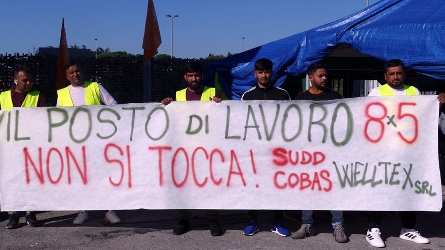 Alcuni operai mostrano uno striscione di protesta davanti alla Welltex dove è iniziato il presidio sindacale (Foto Formichella)