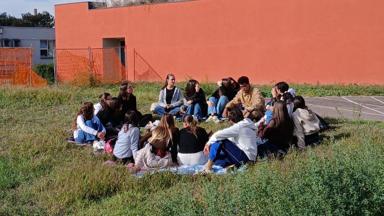 Un gruppo di studenti del liceo Rodari fa lezione nel prato davanti alla scuola