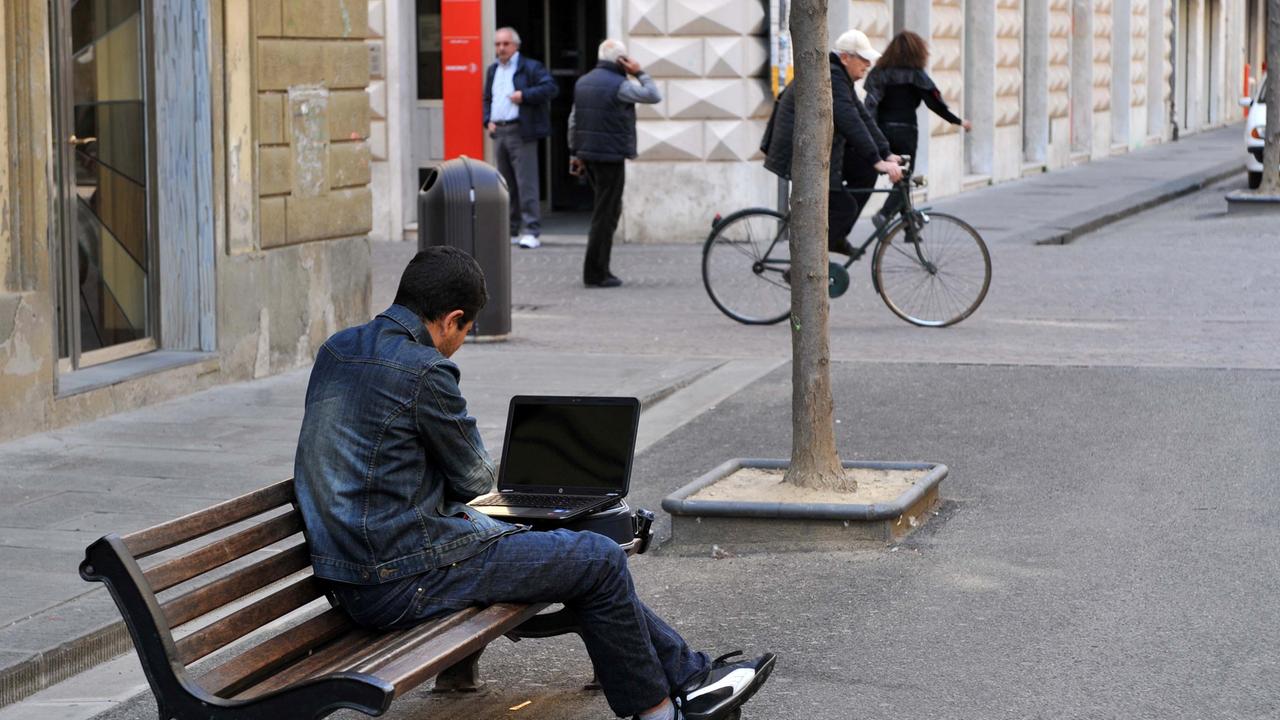Un giovane col pc portatile su una panchina (foto di archivio)