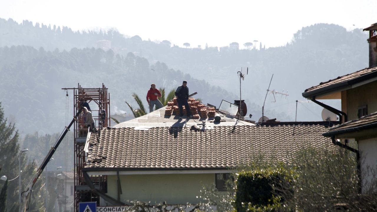 Operai al lavoro sul tetto di una casa danneggiata dalla tempesta di vento