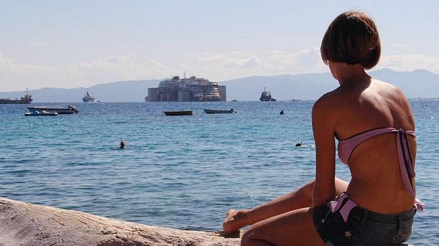 Una ragazza osserva la Concordia al largo del Giglio il giorno della partenza (foto Enzo Russo)