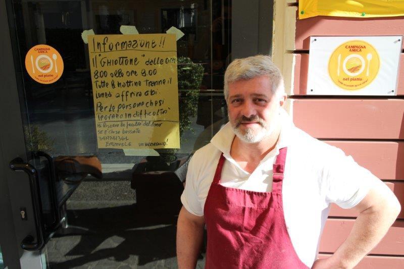 Emanuele Innocenti davanti al suo ristorante, su cui è appeso l'invito rivolto ai bisognosi