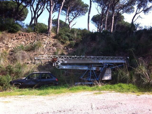 Un'auto e un braccio di una gru abbandonati a lato strada