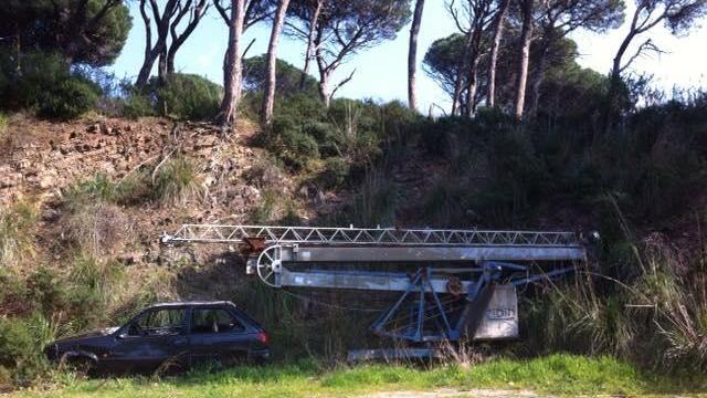 Un'auto e un braccio di una gru abbandonati a lato strada