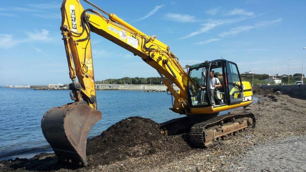 Una scavatrice all'opera sulla spiaggia dei Tre Ponti
