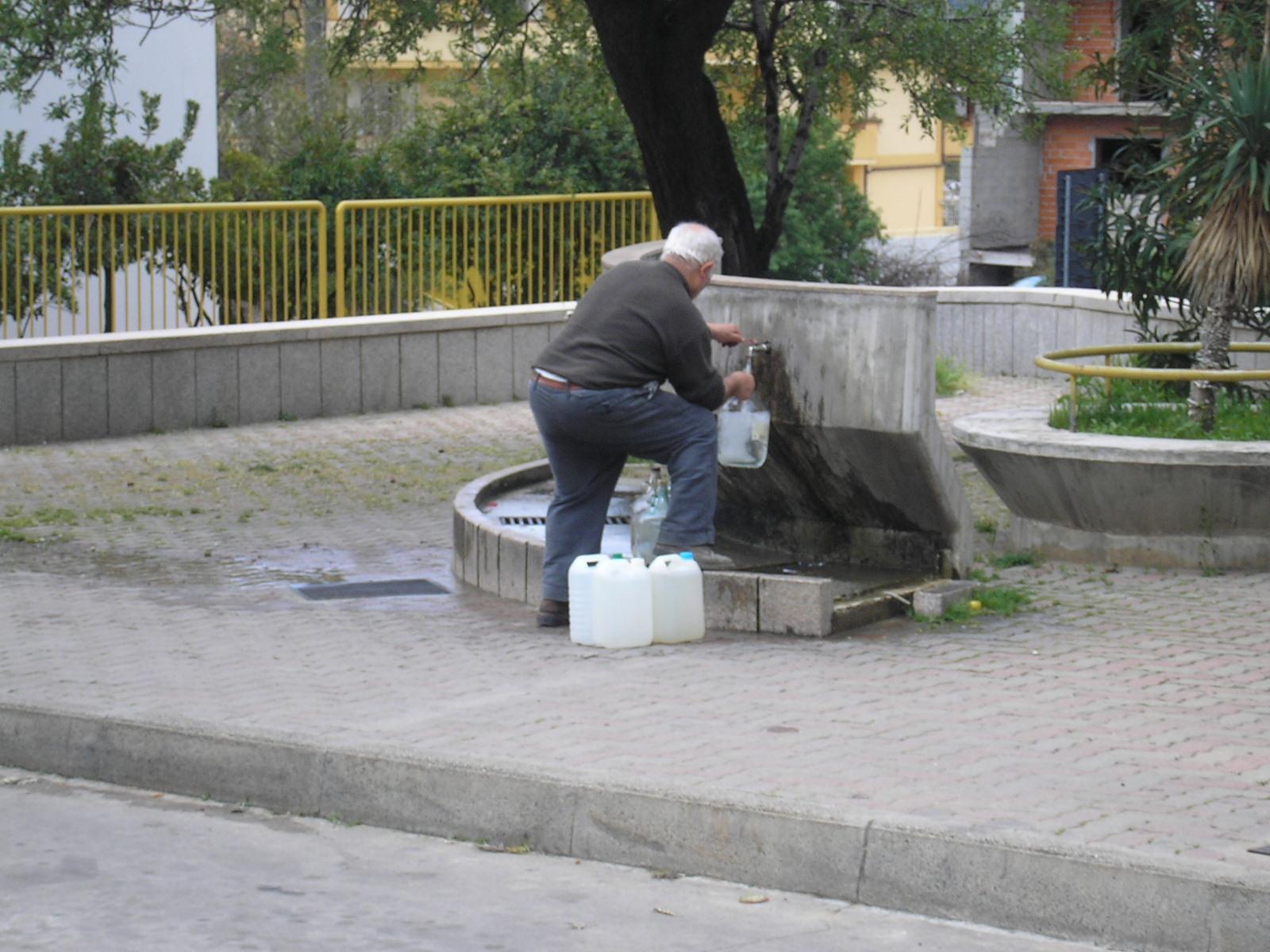 Un anziano si rifornisce di acqua da una fontana