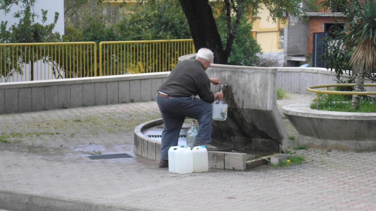Un anziano si rifornisce di acqua da una fontana