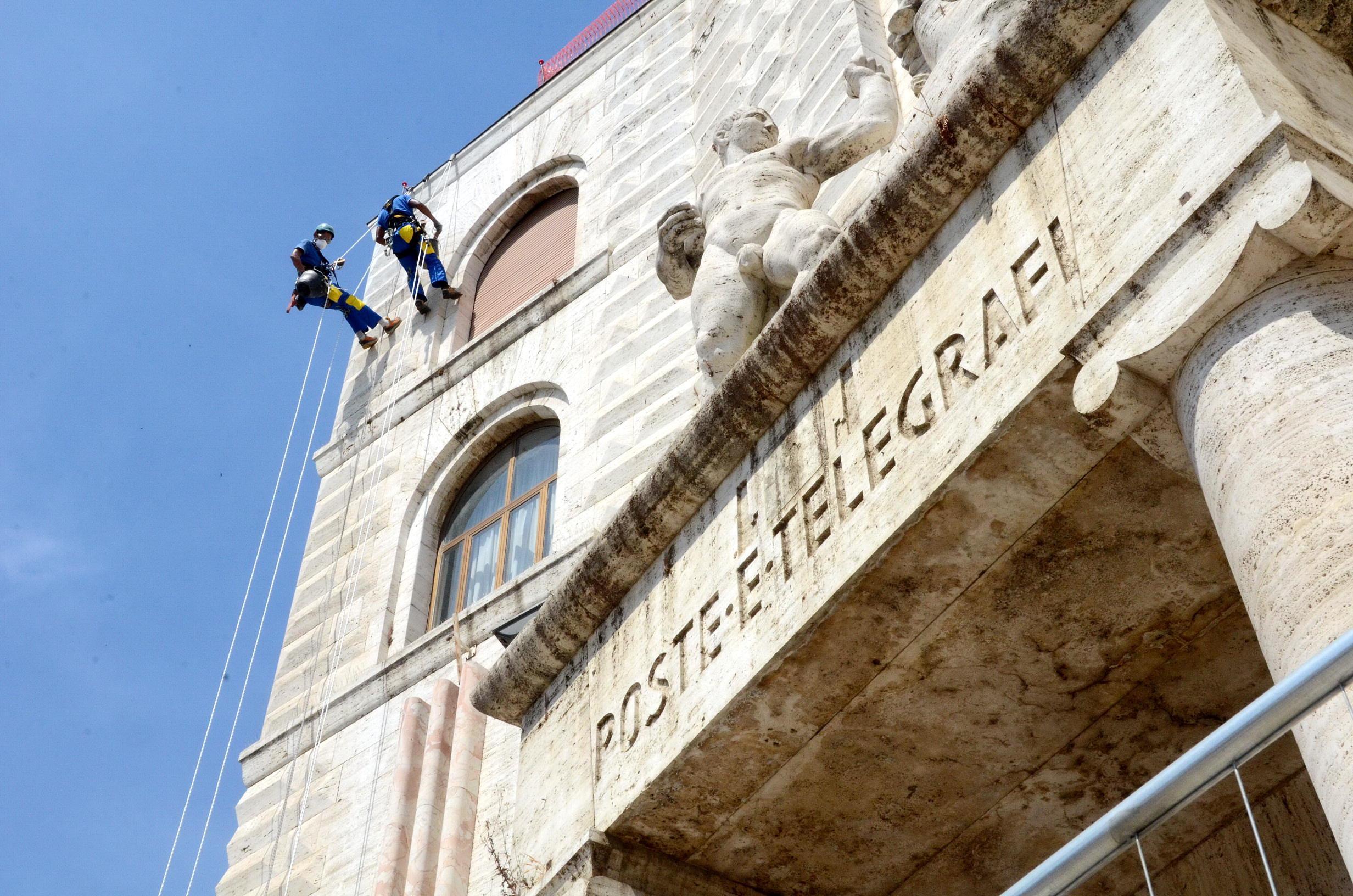 Gli operai acrobati scalano la faccia del Palazzo delle Poste (foto Bf)