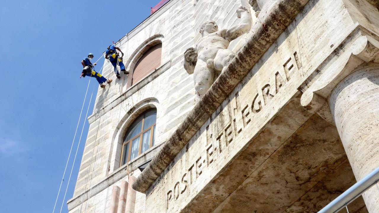 Gli operai acrobati scalano la faccia del Palazzo delle Poste (foto Bf)