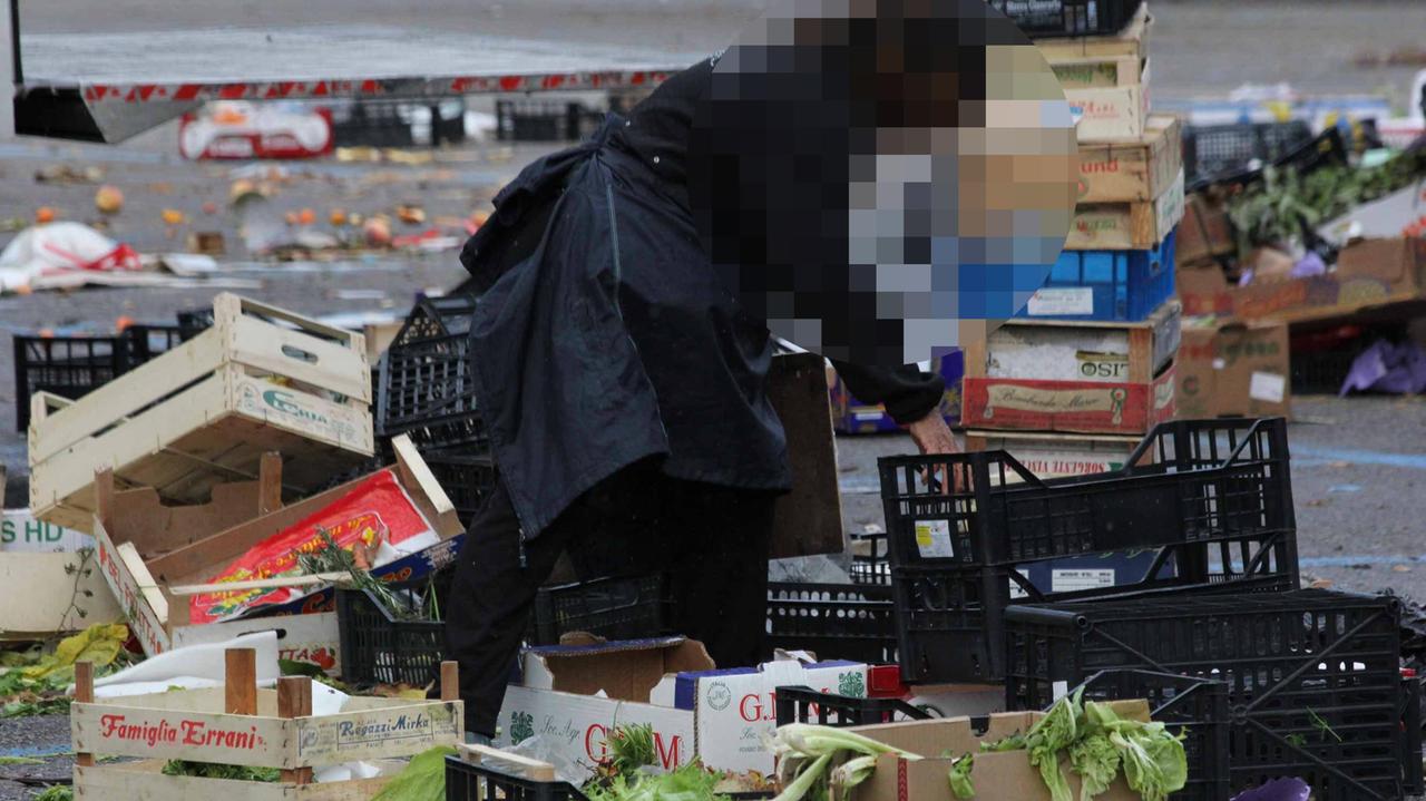 Un'anziana cerca tra la frutta lasciata in piazza dopo il mercato settimanale