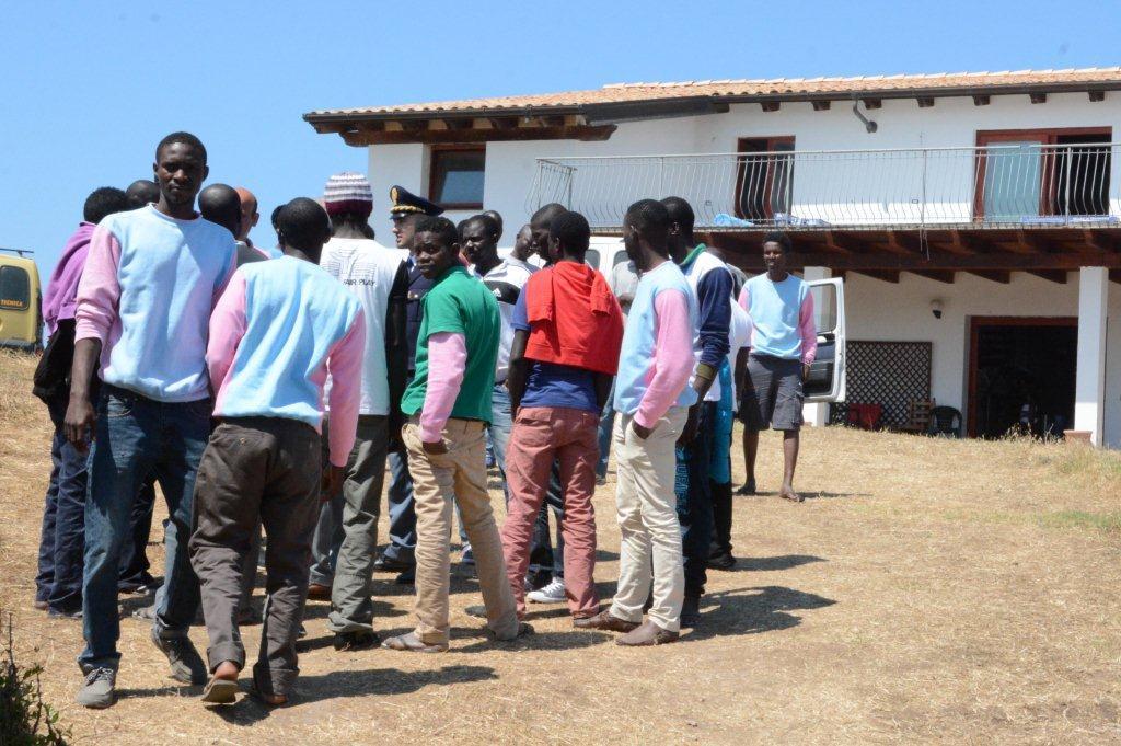 Un gruppo di migranti discute con un agente della polizia nel piazzale davanti al centro accoglienza di Palmadula