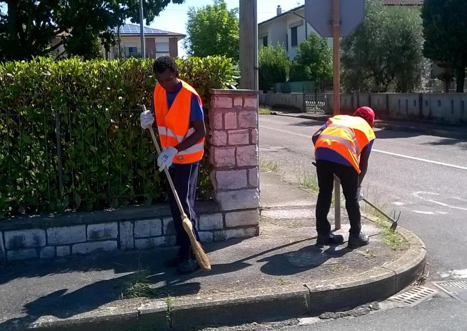Profughi volontari impegnati a ripulire strade e marciapiedi