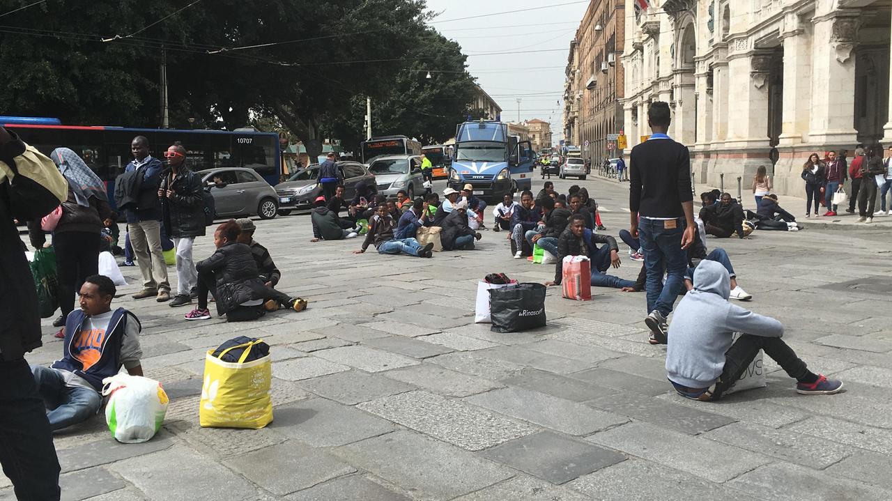 I migranti seduti a terra all'incrocio tra via Roma e il Largo (foto Mario Rosas)