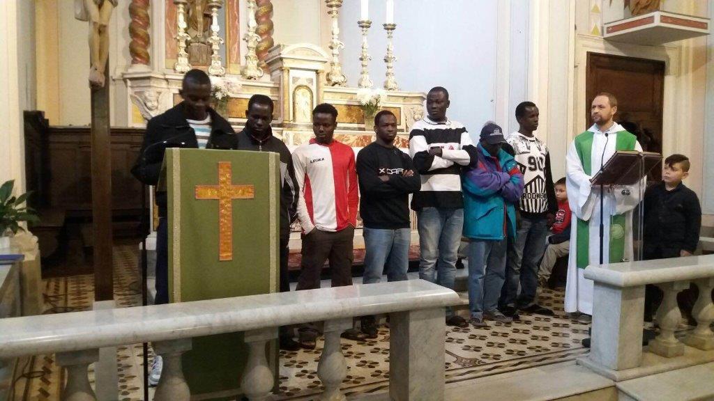 Un gruppo di migranti partecipa alla messa nella chiesa di Marliana insieme a don Alessandro Carmignani (Foto d'archivio)