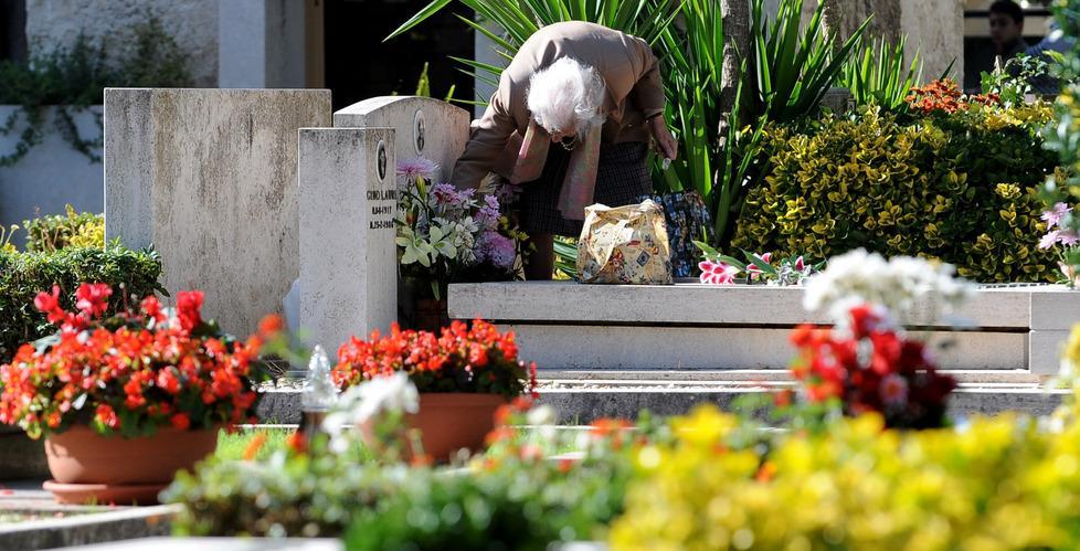 Un'anziana depone dei fiori su una tomba (foto d'archivio)