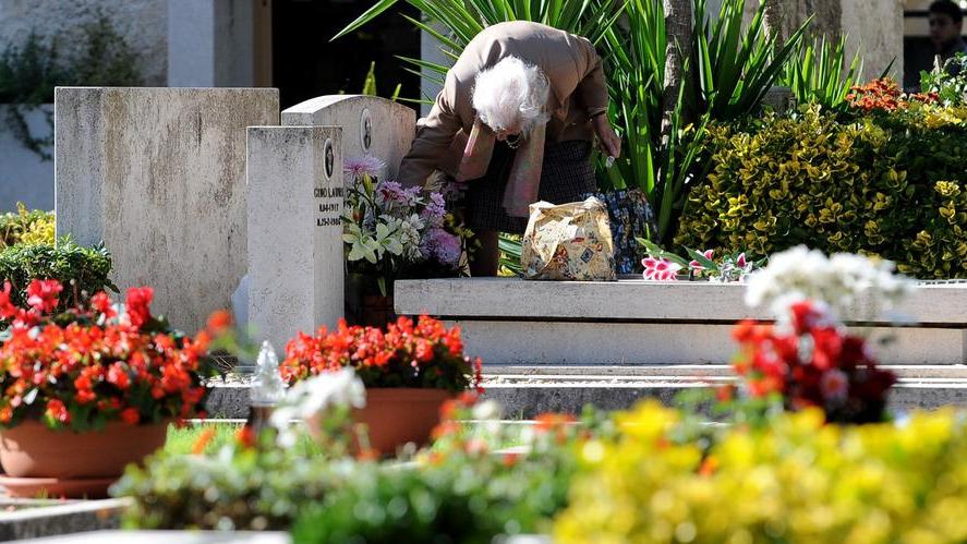 Un'anziana depone dei fiori su una tomba (foto d'archivio)