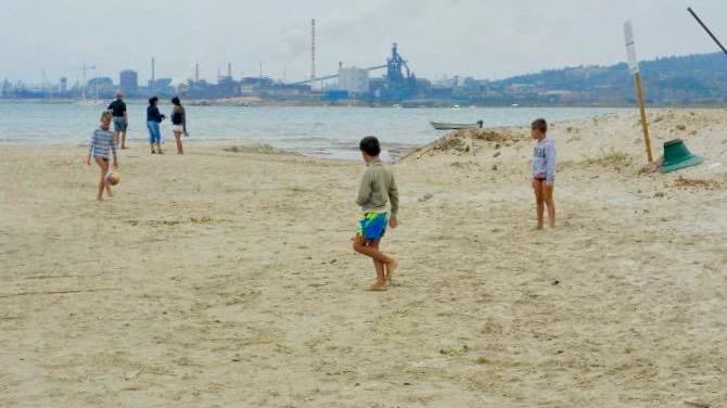 Bimbi giocano sulla spiaggia del Quagliodromo, sullo sfondo la vecchia fabbrica