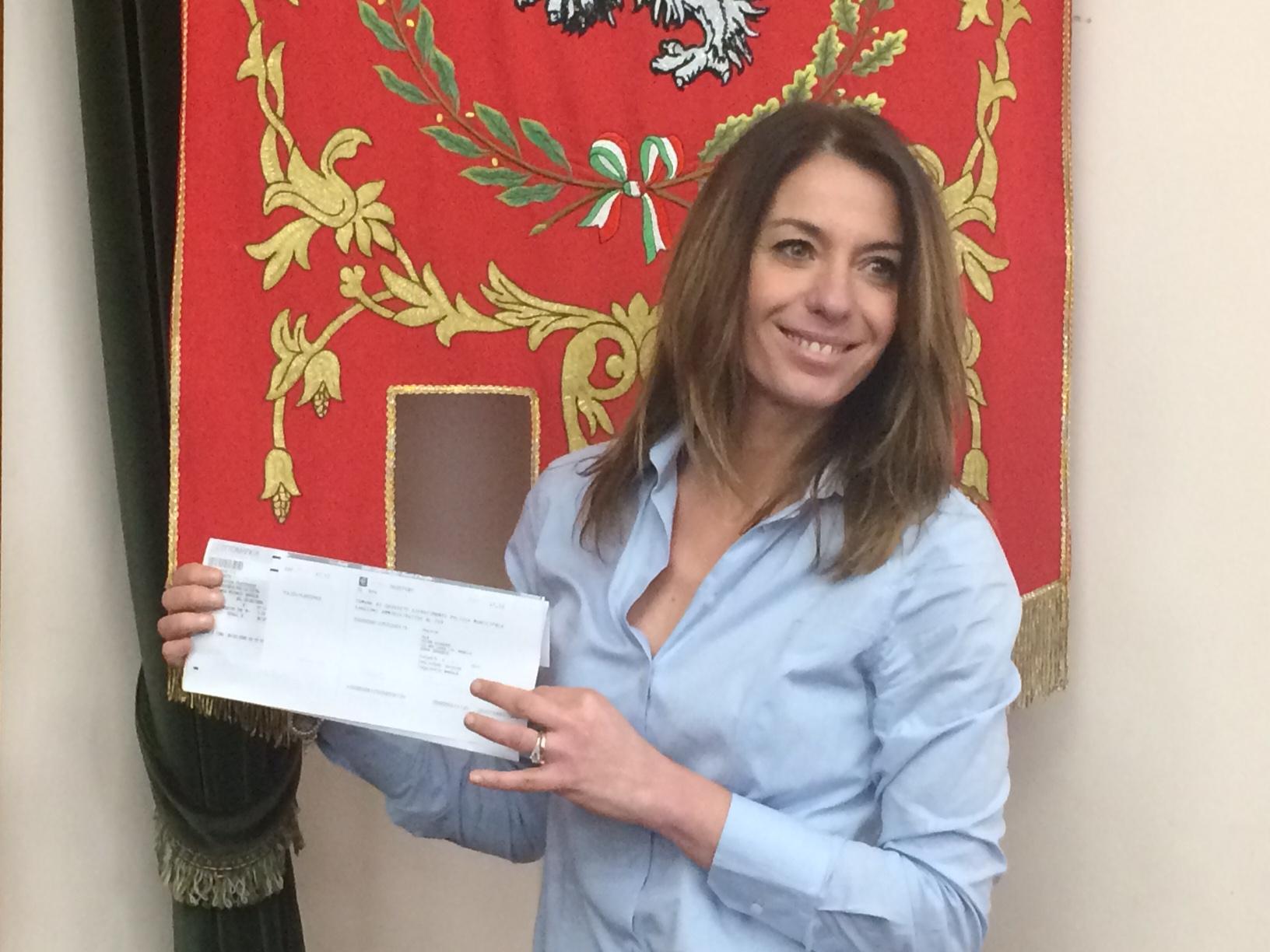 Una sorridente Simona Petrucci, assessora all'ambiente del Comune di Grosseto, mostra un bollettino della Tari