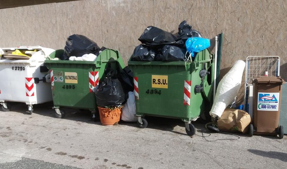 Cassonetti e rifiuti in strada con vista sul ristorante