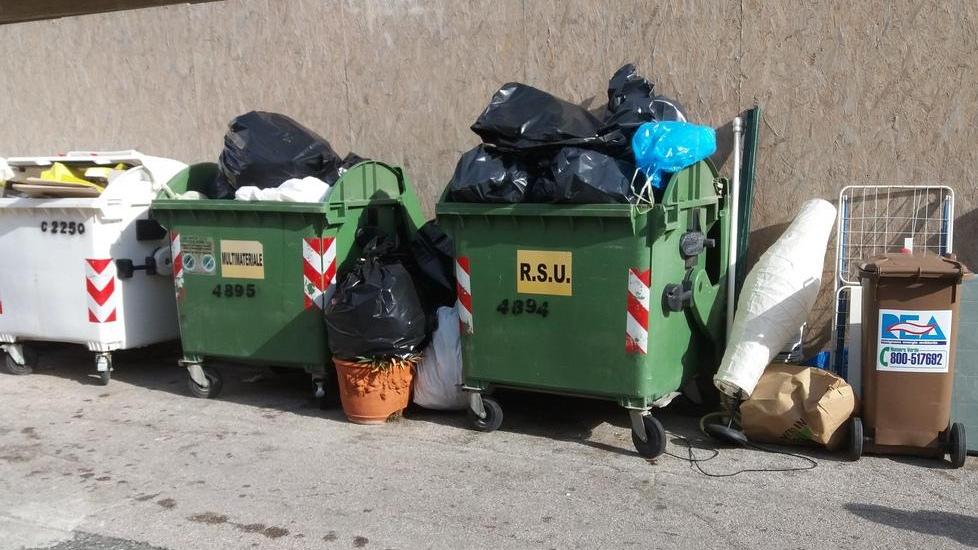 Cassonetti e rifiuti in strada con vista sul ristorante