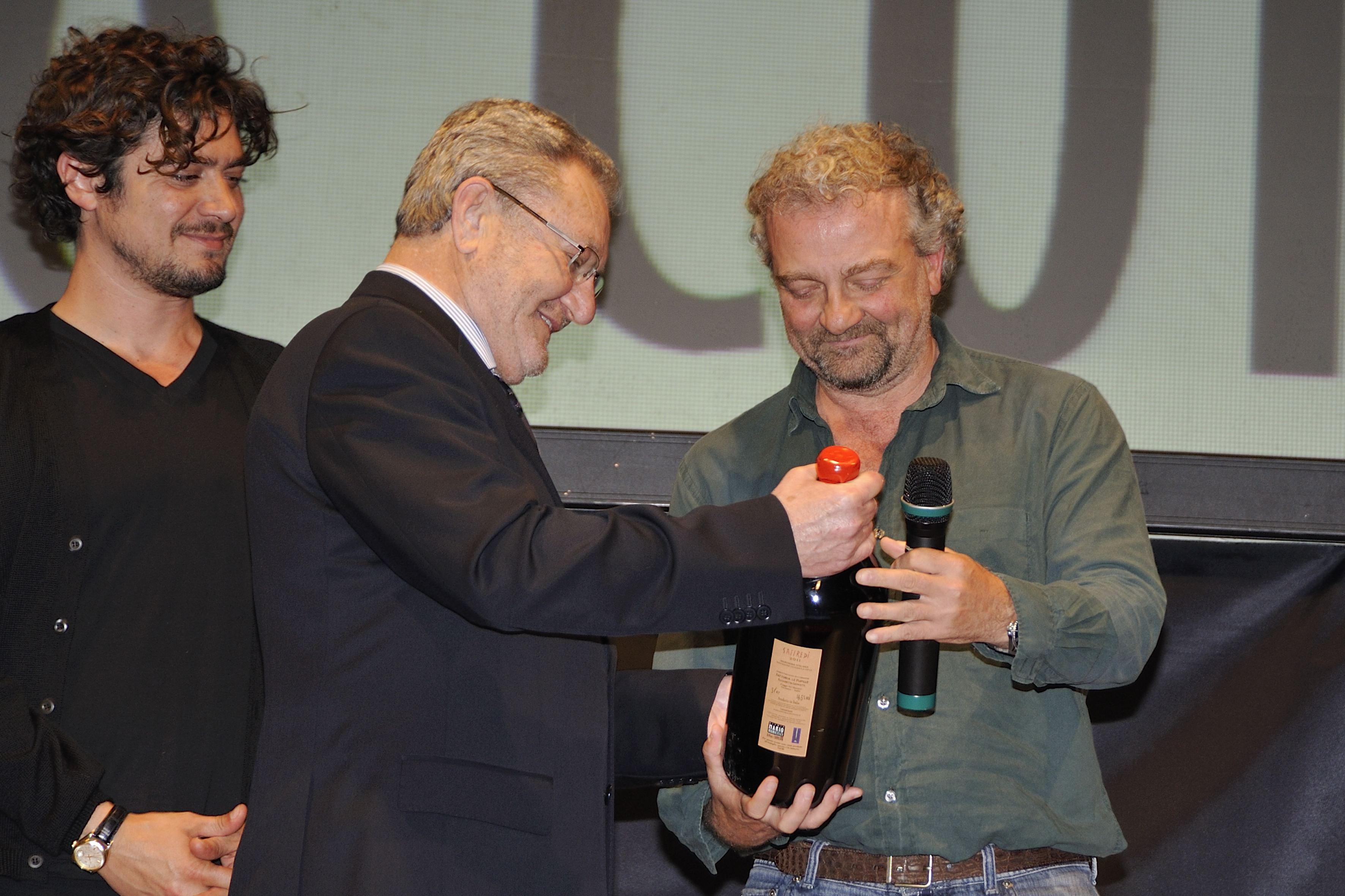 Loriano Valentini, al centro, consegna una bottiglia premio a Giovanni Veronesi durante l'edizione 2014 del Premio Monicelli. Alle sue spalle l'attore Riccardo Scamarcio (foto Agenzia Bf)