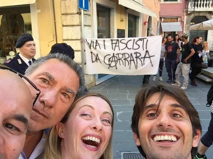 Il selfie di Giorgia Meloni con i contestatori sullo sfondo