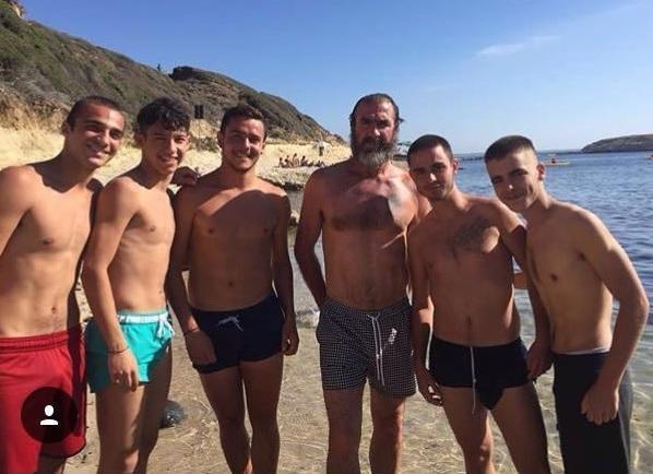 Eric Cantona assieme ad alcuni ragazzi nella spiaggia di S'Archittu