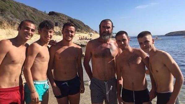 Eric Cantona assieme ad alcuni ragazzi nella spiaggia di S'Archittu
