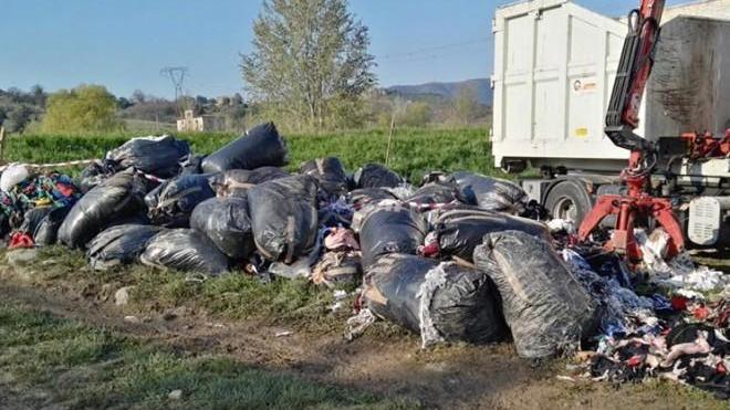 Sacchi neri pieni di scarti tessili abbandonati in un campo