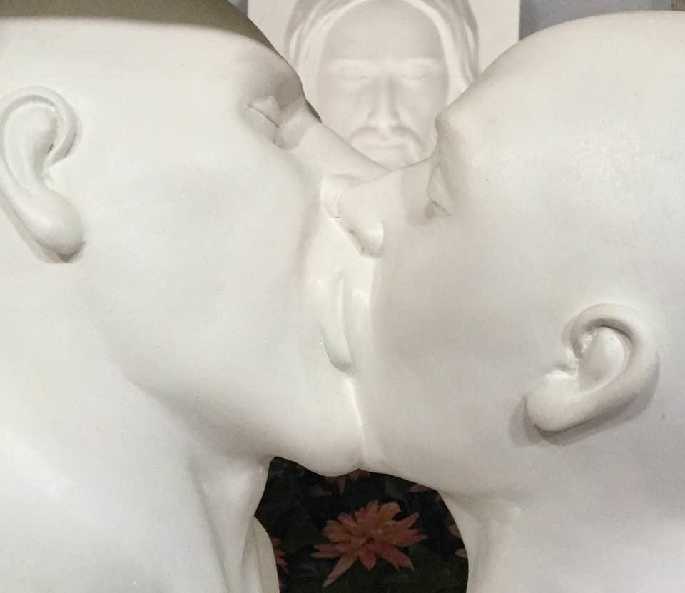 La scultura con il bacio gay quando era in chiesa con dietro un ritratto di Cristo