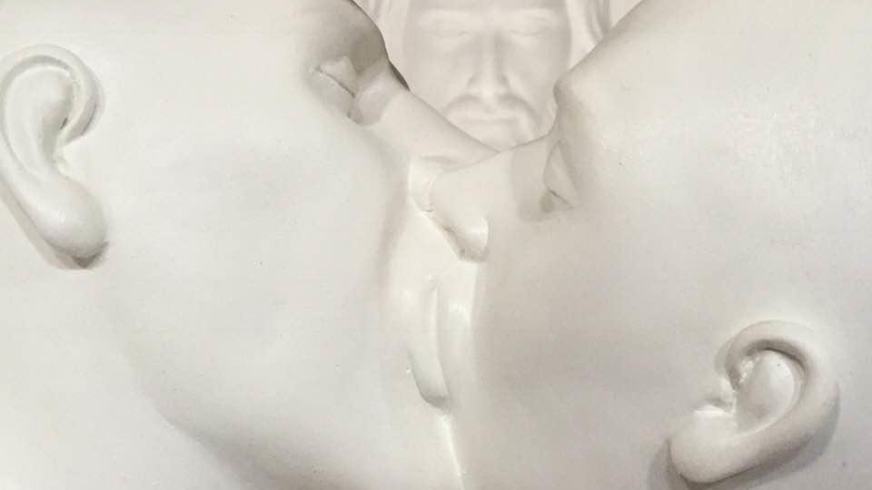 La scultura con il bacio gay quando era in chiesa con dietro un ritratto di Cristo