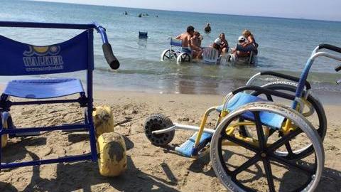 In primo piano le sedie a rotelle utilizzate sulla spiaggia e i ragazzi in acqua insieme ai volontari