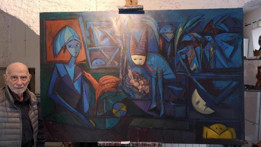 Julio Silva vicino a un grande suo quadro nell'ingresso della casa