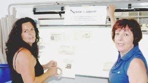 Due artigiane affiggono articoli di giornale sulla crisi del tessile
