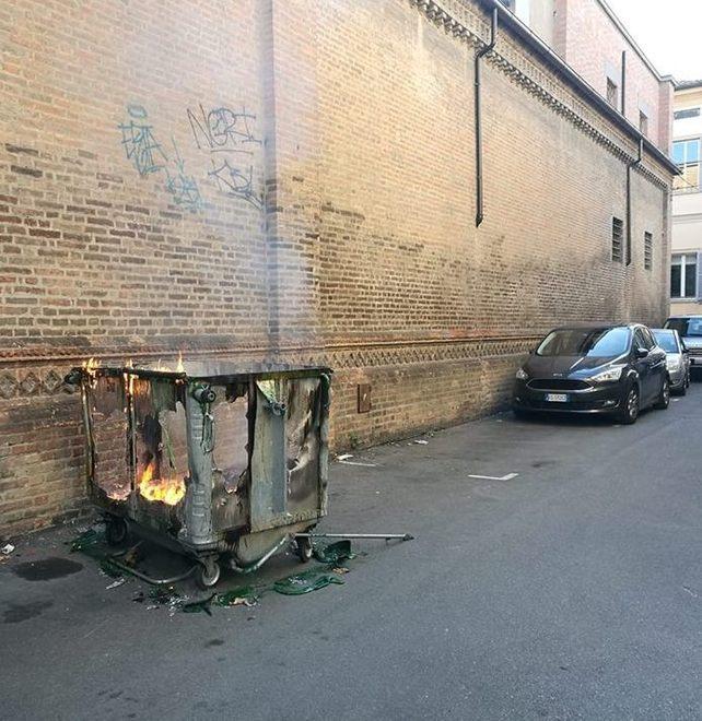 Cassonetto a fuoco accanto alle auto