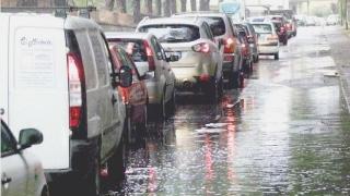 Sopra, una mamma e sua figlia sotto la pioggia ai lati le auto in coda per entrare in città alla ricerca di un posto dove parcheggiare l’auto