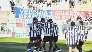 Paco, il cagnolino mascotte del vice presidente del Cecina e, a fianco, giocatori biancoblù festggiano dopo il gol vittoria