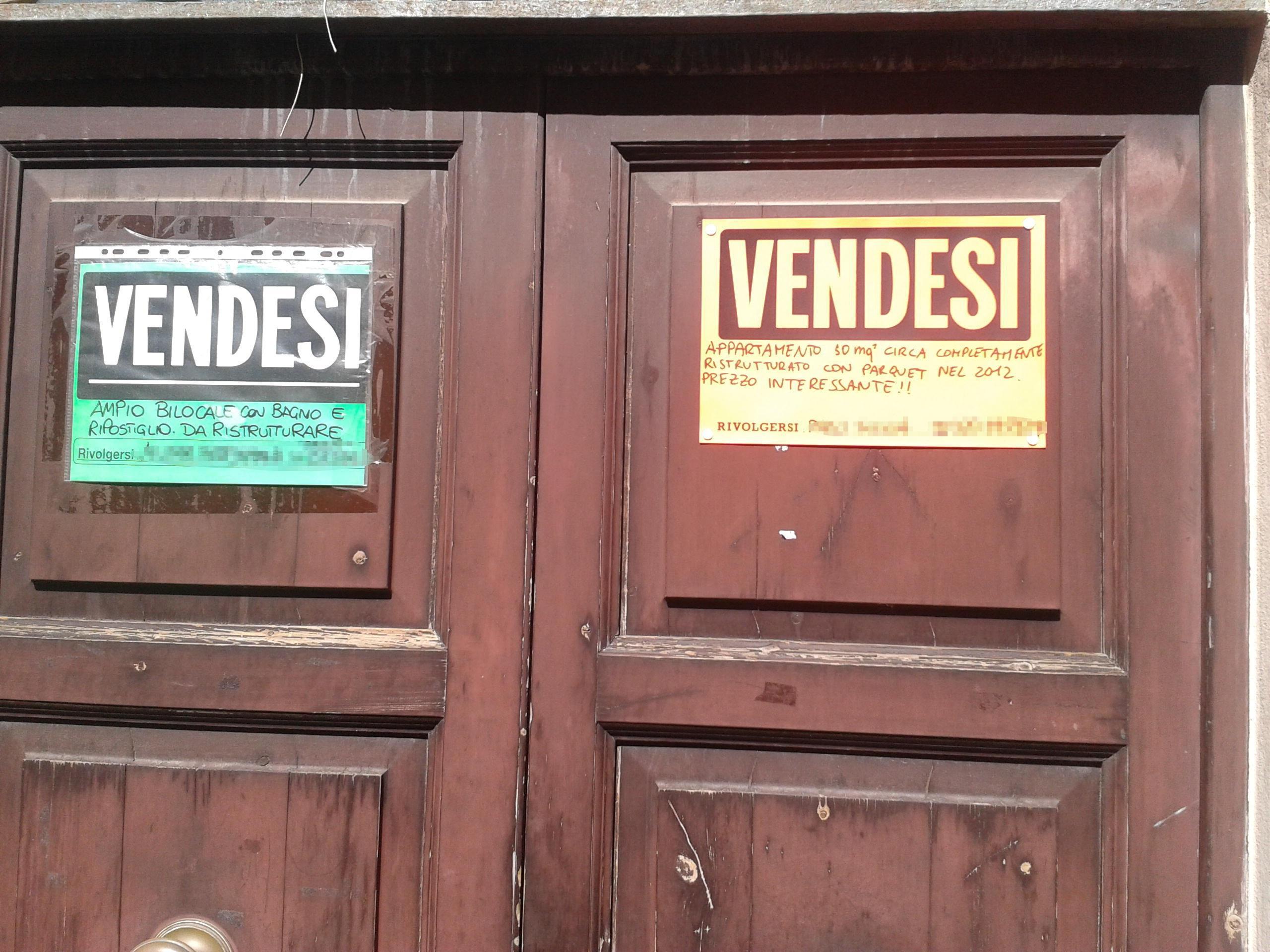 Un doppio cartello "vendesi" sul portone di un palazzo