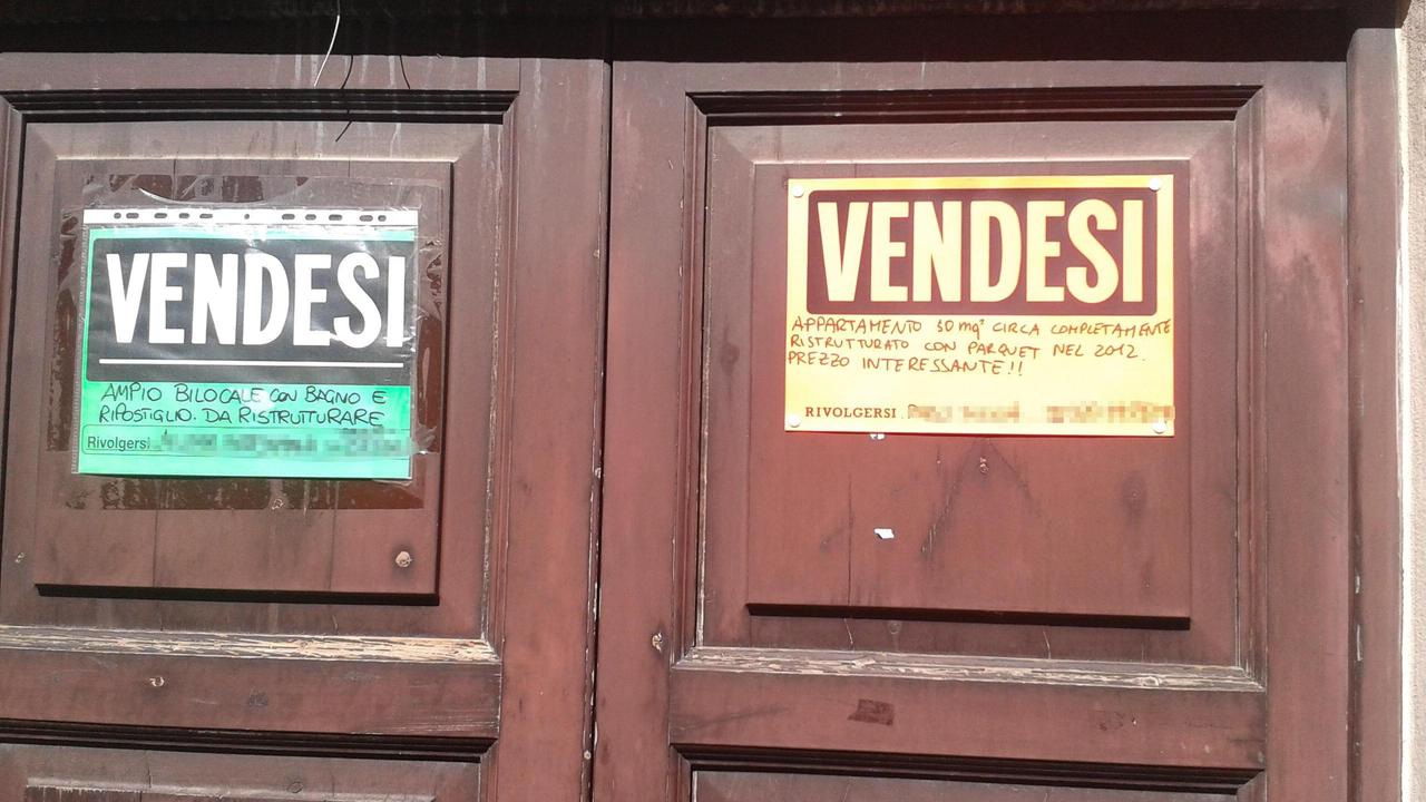 Un doppio cartello "vendesi" sul portone di un palazzo