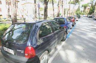 Alcune auto parcheggiate negli stalli blu; a destra lo shopping natalizio in centro