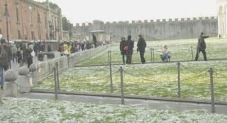 Il prato di piazza dei Miracoli spruzzato di neve e sotto un mezzo dei vigili del fuoco al lavoro in strada