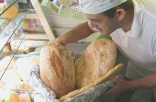 Un panettiere porta sul bancone del pane fresco appena sfornato