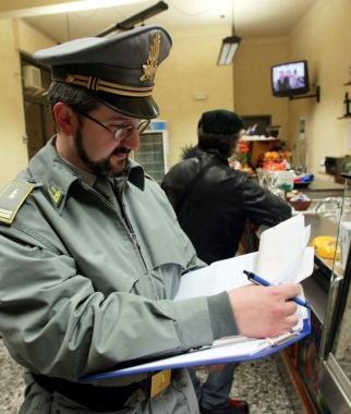A sinistra il cartello di chiusura temporanea affisso nei negozi sorpresi per 4 volte a non emettere scontrino o ricevuta fiscale; a destra un finanziere al lavoro     