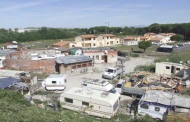 Sopra, unimmagine del villaggio e del campo visti dallalto. Nella foto grande, rom al cancello presidiato dai vigli urbani 