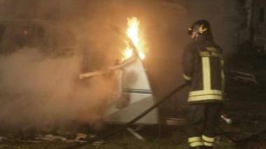 A sinistra, un vigile del fuoco spenge l’incendio; a destra, proprietari dei camper in attesa e mezzi distrutti